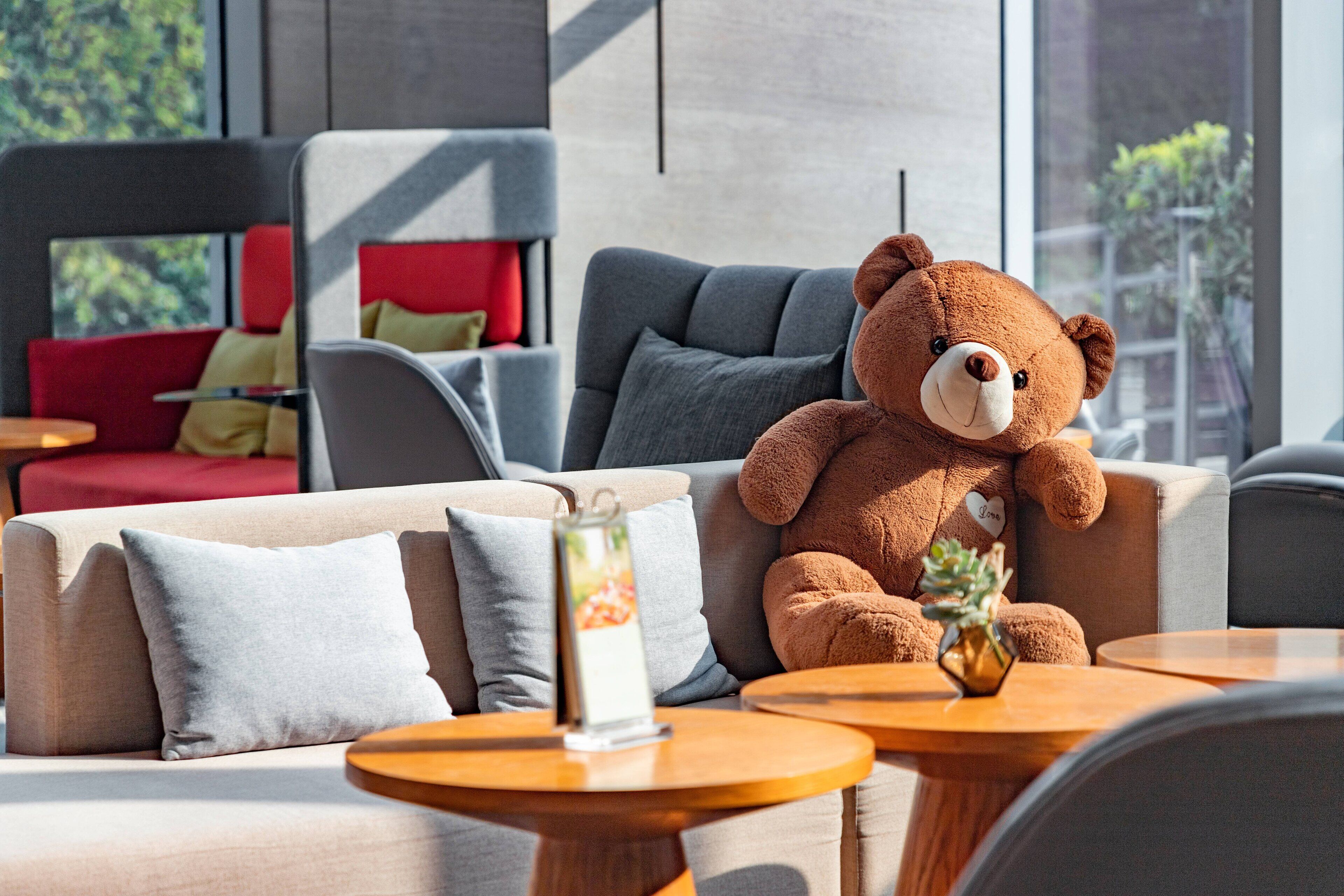 A cozy seating area with a plush brown teddy bear, a vase with a plant, and a small table with a menu stand.