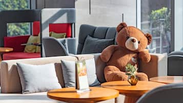 A cozy seating area with a plush brown teddy bear, a vase with a plant, and a small table with a menu stand.