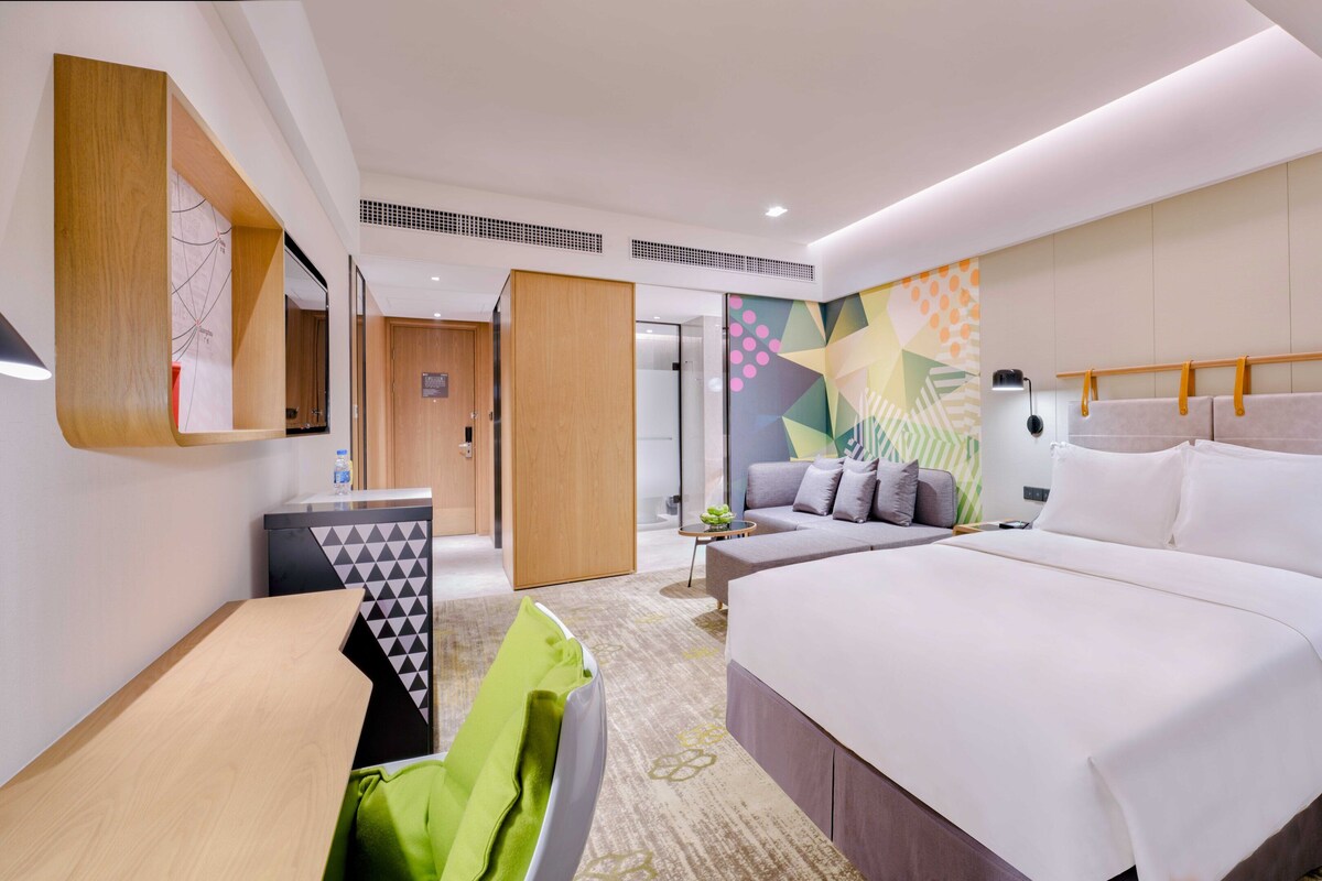 A modern hotel room with a large bed, a desk, and a seating area.