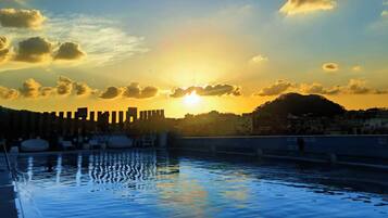 Una piscina en la azotea con un horizonte urbano al atardecer.