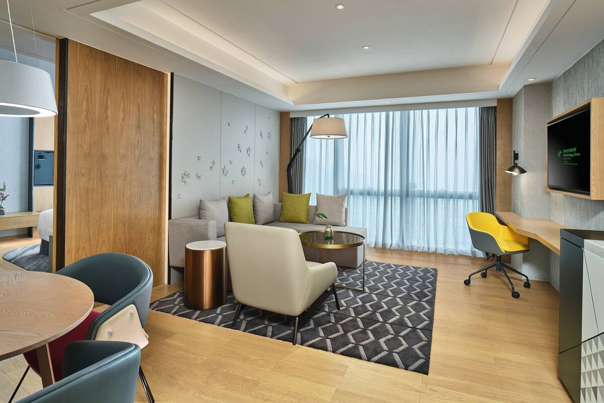 A modern hotel room with a dining area, a sofa set, a round table, and a TV mounted on the wall.