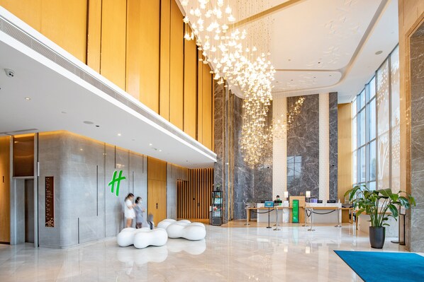 A modern lobby with a reception desk, seating area, and a large chandelier.
