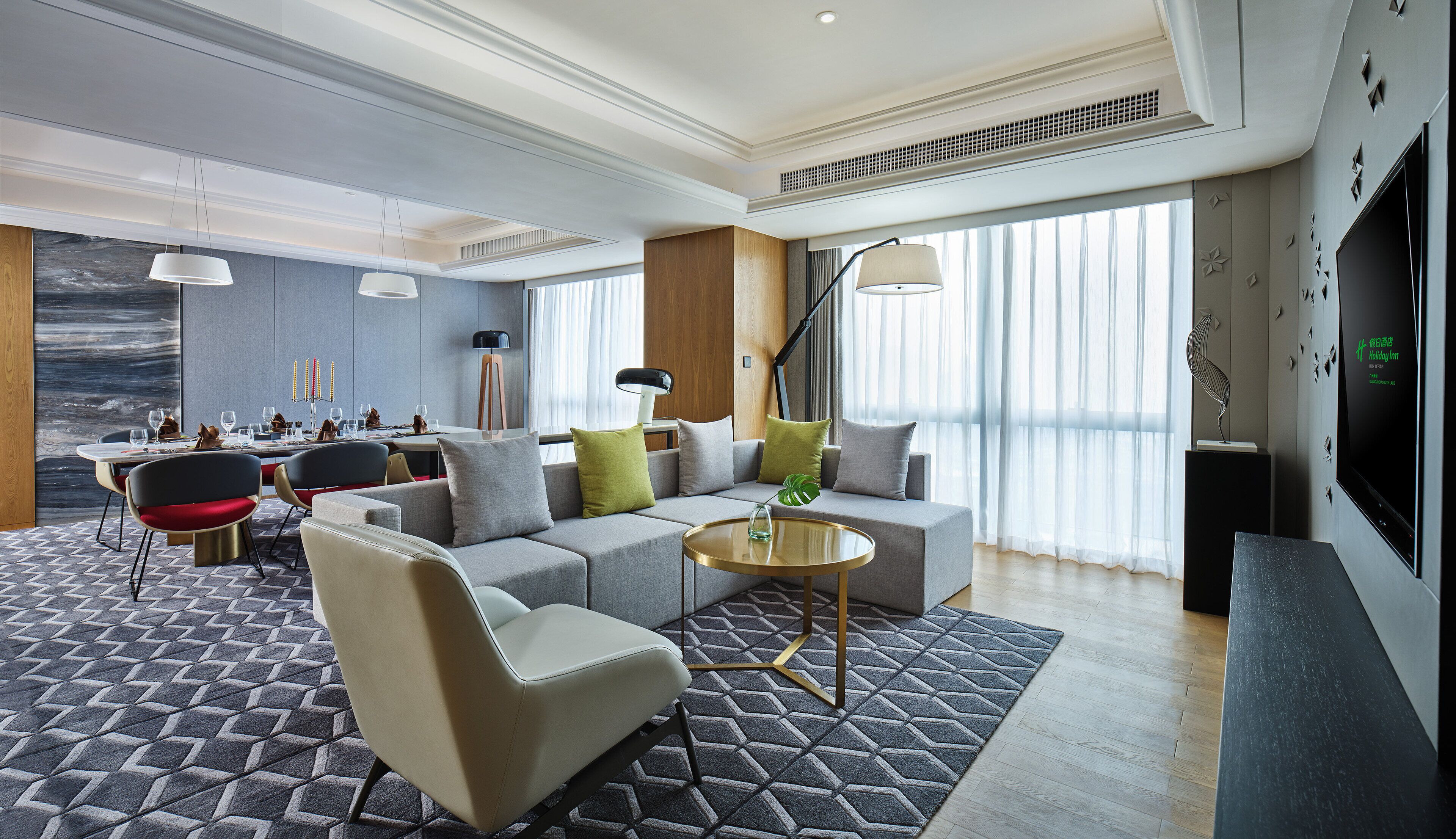 A modern hotel room with a dining area, a sofa set, a TV, and a large window with curtains.