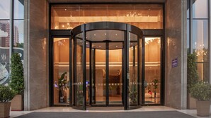 Entrada de hotel com porta giratória, portas de vidro e vista do interior.
