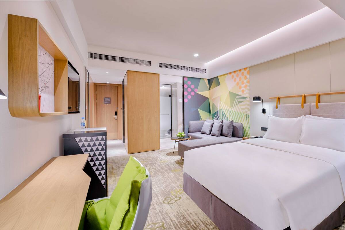 A modern hotel room with a large bed, a desk, and a seating area.