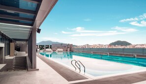 A modern rooftop pool with clear blue water, a view of a cityscape, and a mountain in the background.