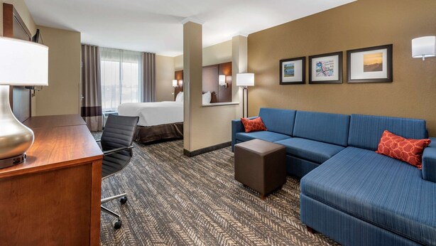 A hotel room with a bed, a blue sofa, a desk with a lamp, and a carpeted floor. - Comfort Suites Dry Ridge (Dry Ridge)