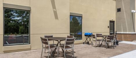 An outdoor patio area with tables and chairs, large windows, and a barbecue grill.