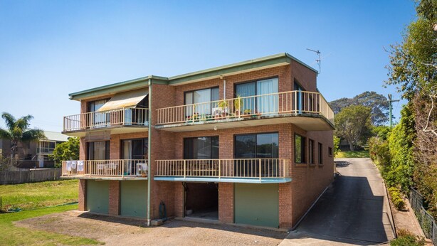 Un immeuble résidentiel de deux étages doté d’un balcon à l’étage supérieur, d’un garage à l’avant et d’une allée menant à la rue.