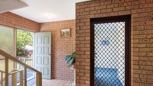 Un couloir avec un mur en briques, une porte blanche et une porte vitrée donnant sur l’extérieur.