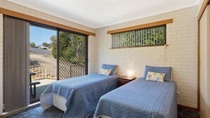 Une chambre avec deux lits, une fenêtre donnant sur l’extérieur et un balcon avec une balustrade.