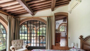 A bedroom with a large bed, a chair, and a view of a patio area. - Bouganville by Interhome (Bibbona)