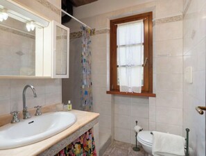 Un baño con lavamanos, espejo, cortina de ducha, inodoro y ventana.