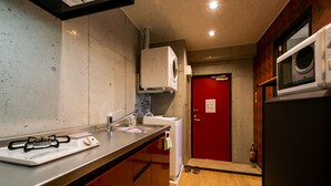 Een kleine keuken met een gasfornuis, een magnetron, een wasmachine en een rode deur.