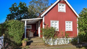 Una casa di legno rossa con un portico bianco e un piccolo giardino.