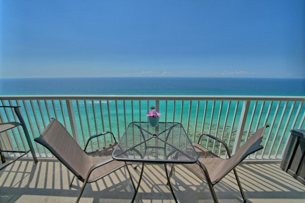 A balcony with a table and chairs overlooking a turquoise sea.