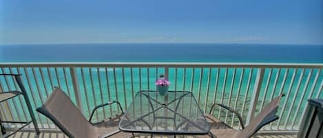 A balcony with a table and chairs overlooking a turquoise sea.