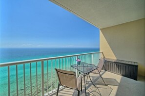 Varanda com vista desimpedida para o oceano, duas cadeiras e uma mesa pequena.