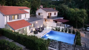 Ein modernes, zweistöckiges Haus mit Swimmingpool, Sitzgelegenheiten im Freien und einer Treppe, die zu einem Balkon führt.