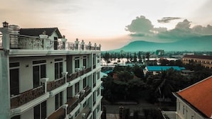 A multi-story building with balconies, a courtyard, and a view of a river and distant mountains. - Intanou Boutique Hotel Kampot (Kampot)