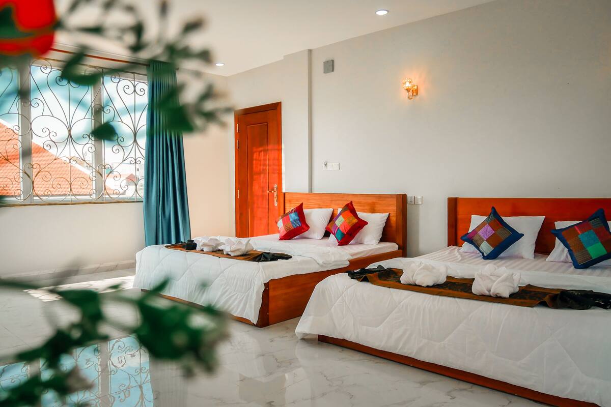 A hotel room with two beds, a wooden headboard, and a window with decorative iron bars.