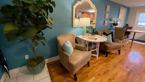 Una sala de estar con una planta grande, dos sillones, una mesita y un espejo en la pared.