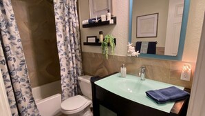Un baño con bañera, inodoro y lavabo. Hay repisas sobre el lavabo y un espejo también sobre él.