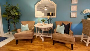 Una habitación con dos sillones, una mesita redonda, un espejo y una planta en maceta.