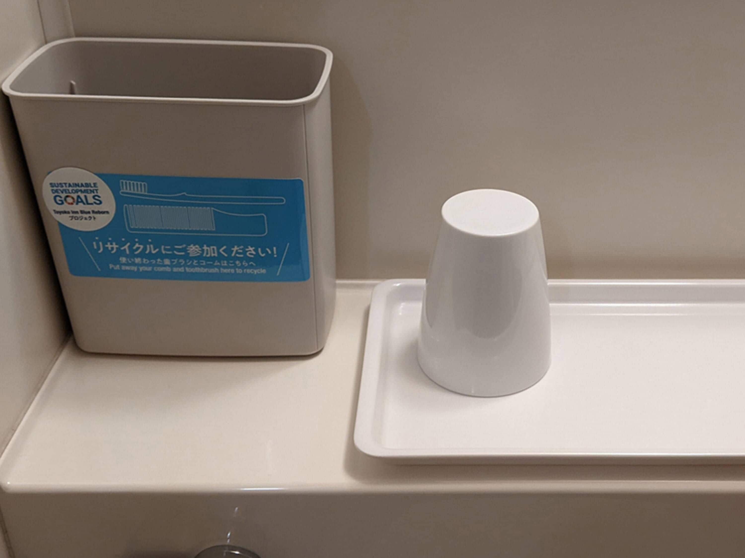 A trash bin with a recycling label and a white cup on a tray.
