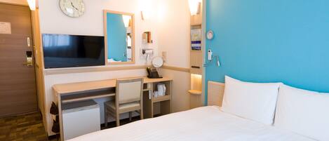 Habitación de hotel con cama, escritorio, silla, televisor, equipo de aire acondicionado y un reloj en la pared.