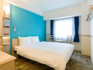 A hotel room with a large bed, a bedside table, a small desk, a chair, a window with curtains, and a wall-mounted lamp. - Toyoko Inn Joetsumyoko-eki Nishi-guchi (Joetsu)