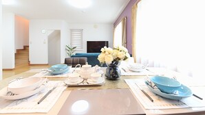Ein Essbereich mit Tisch für vier Personen, einem Blumenstrauß und einer Couch im Hintergrund.