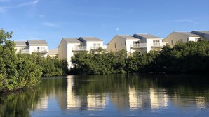 A row of modern, single-story buildings with a calm water body in the foreground, reflecting the structures.