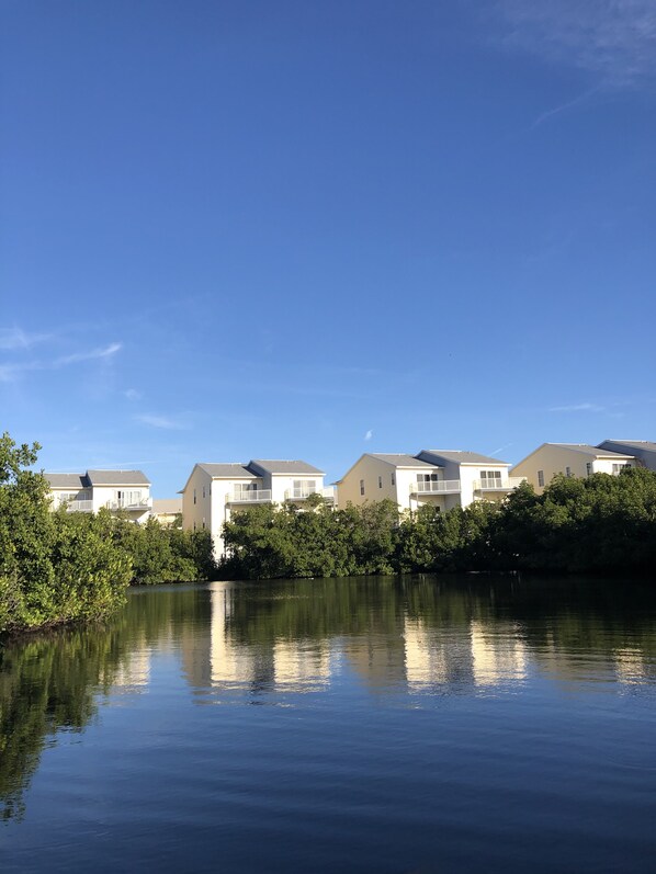 A row of modern, single-story buildings with a calm water body in the foreground, reflecting the structures.