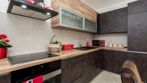 A modern kitchen with dark cabinets, a wooden countertop, a built-in microwave, and a red kettle on the shelf.