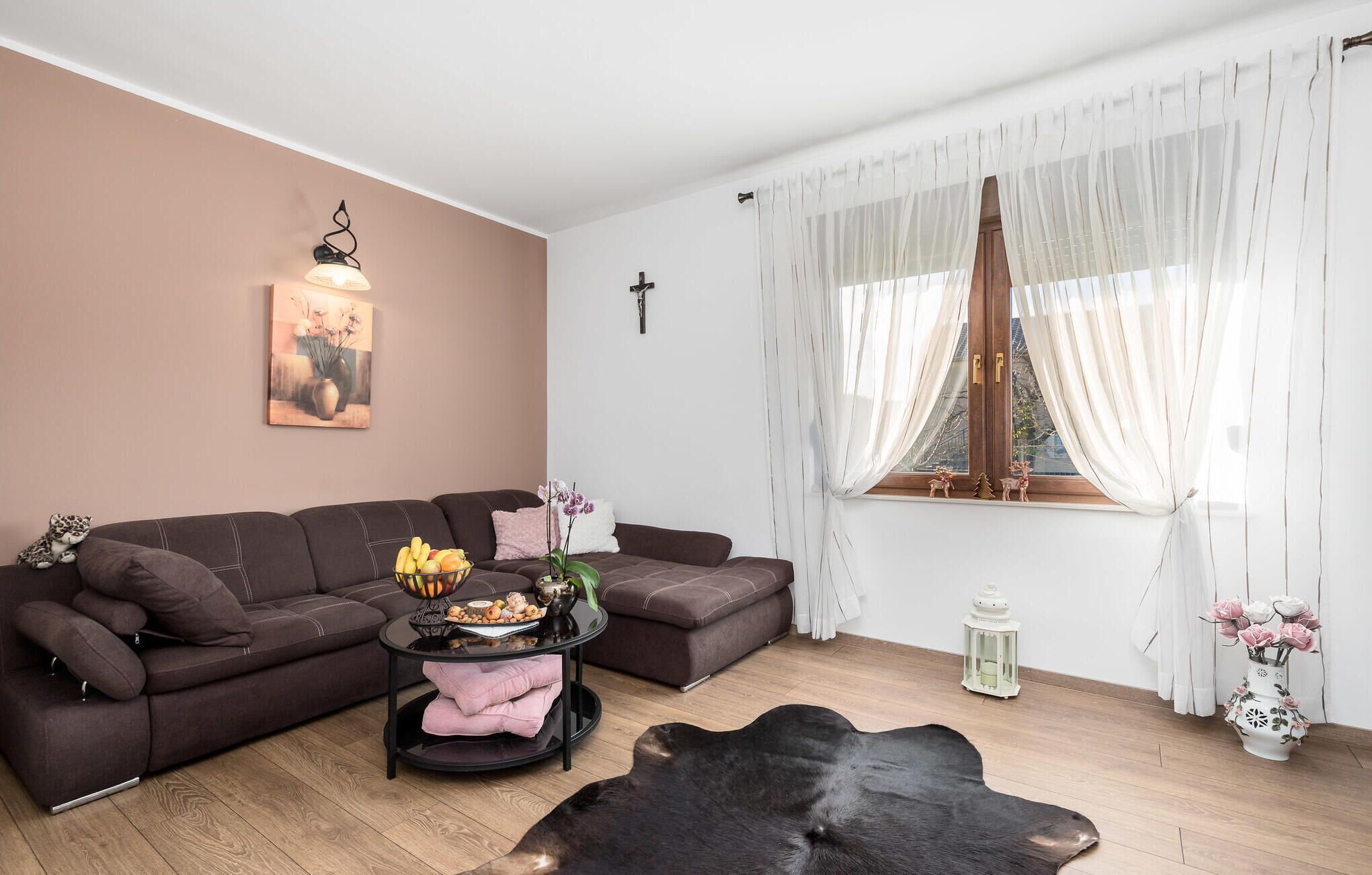 A living room with a brown sofa, a black coffee table, a white vase with flowers, and a wooden cross on the wall.