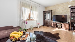 A living room with a sofa, a glass coffee table with fruit, a leather rug, a TV, and a stone wall.