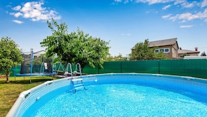 A clear blue swimming pool with a ladder, surrounded by a green fence and trees.