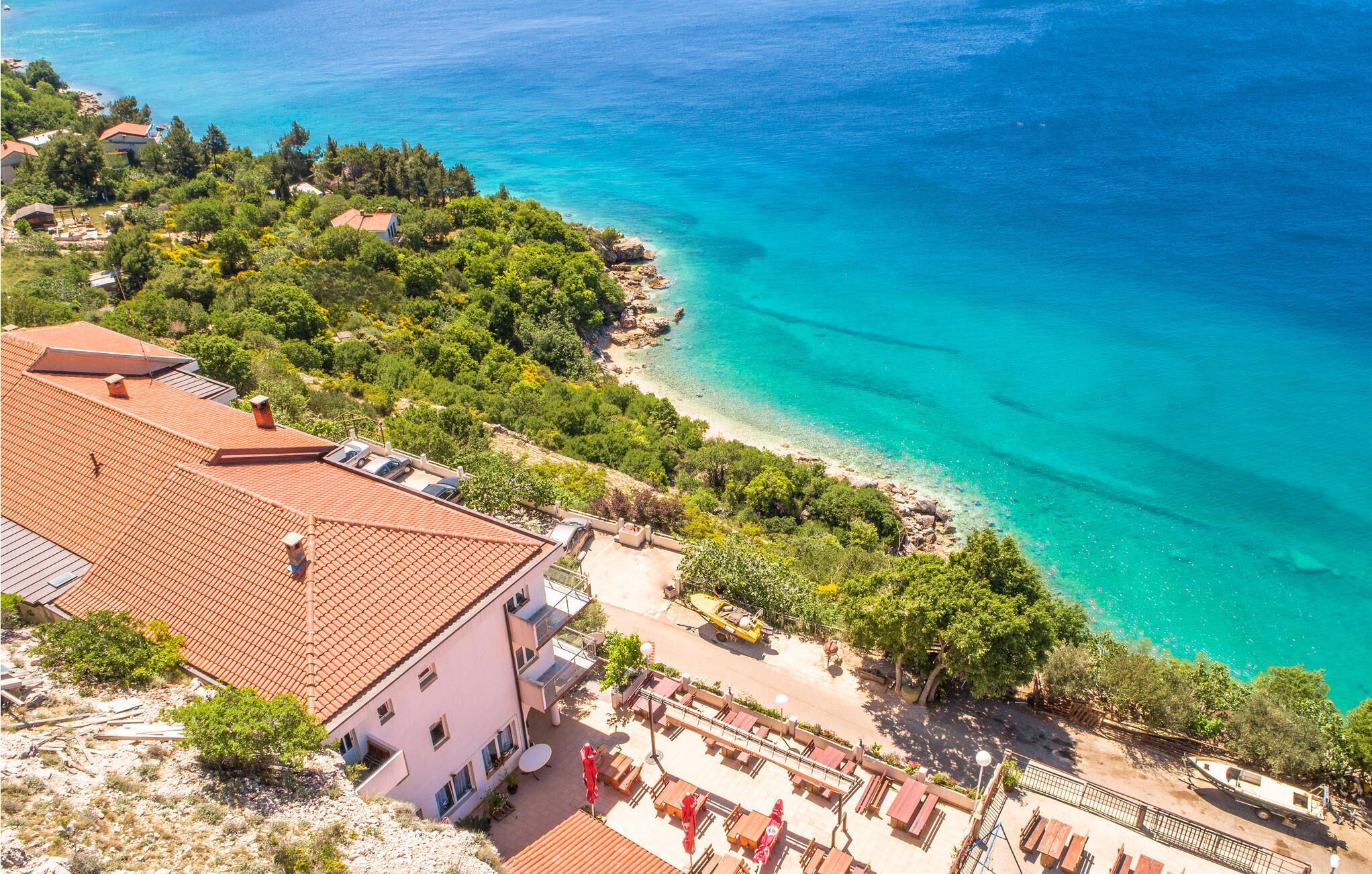 Une propriété située sur la côte, dotée d’un patio, offrant une vue sur la mer et comprenant un bâtiment avec un toit recouvert de tuiles rouges.