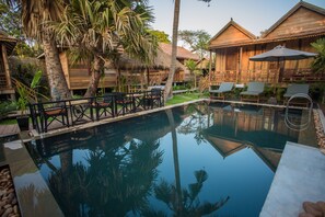Ein Poolbereich mit Holzhütten, Liegestühlen und einem Pool, der die Umgebung spiegelt.