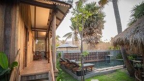 Une maison en bois avec une piscine, du mobilier d’extérieur et un toit de chaume.