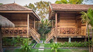 Une cabane en bois avec un toit de chaume, une terrasse en bois et un escalier menant à un porche abrité.
