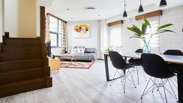 A modern living room with a staircase, a dining area with black chairs, a sofa with patterned cushions, and a large painting on the wall. - FC House Shibuya No.1 (Tokyo)