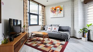 A modern living room with a sofa, a coffee table, a TV on a wooden stand, and a large window with curtains. - FC House Shibuya No.1 (Tokyo)