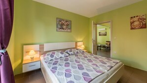 A bedroom with a bed, two bedside lamps, a nightstand, a door, and a wall with a painting.