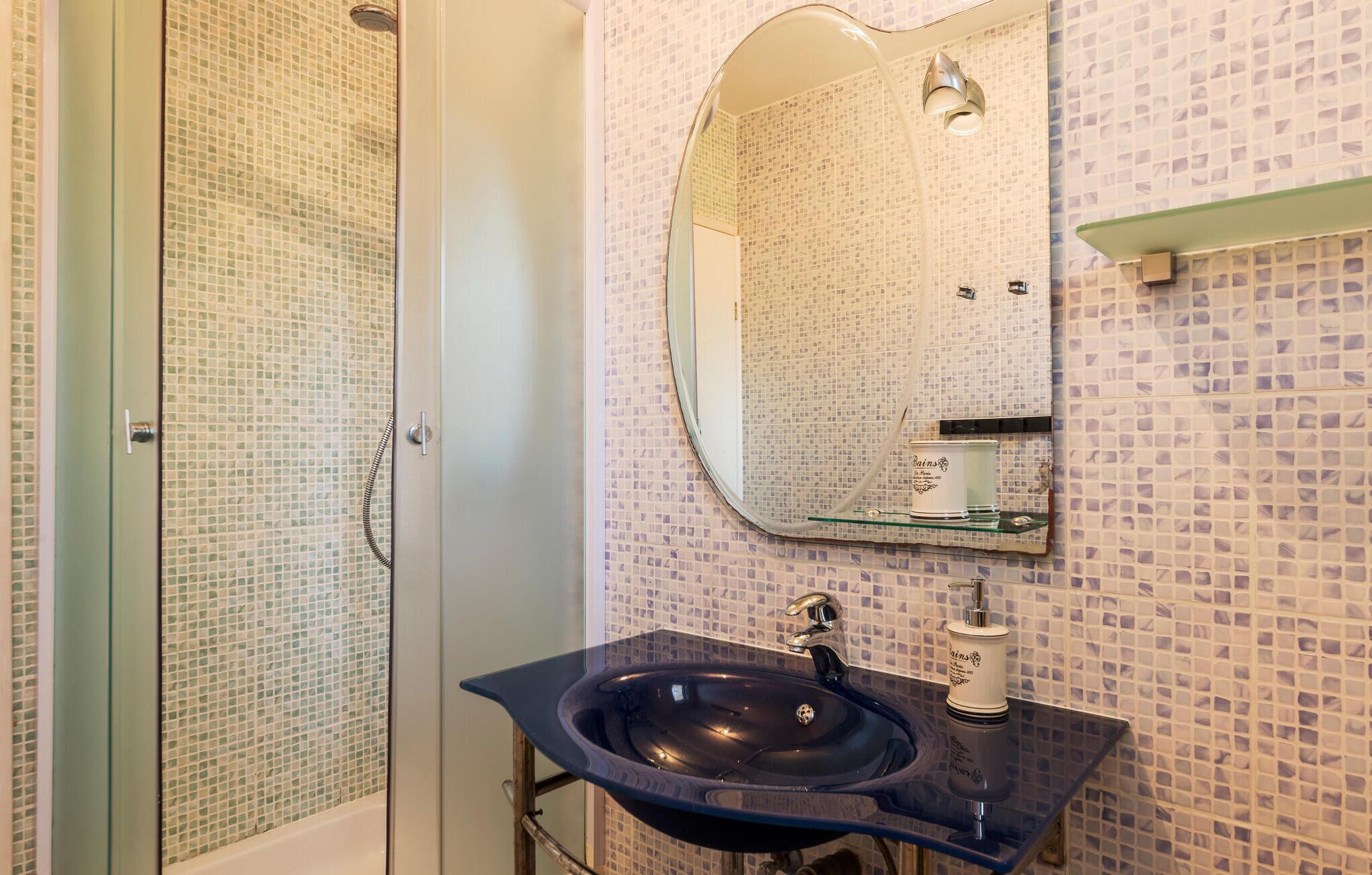 A bathroom with a glass shower enclosure, a sink with a mirror above it, and a tiled wall.