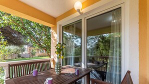 A balcony with a wooden table, two purple mugs, and a vase with green leaves.