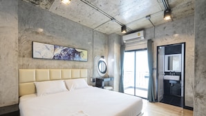 Une chambre d’hôtel moderne avec un grand lit, un miroir rond, une salle de bain avec un lavabo et une vue sur l’extérieur.