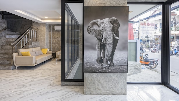 Un hall d’entrée moderne avec un sol en marbre, un canapé beige agrémenté de coussins jaunes, une grande œuvre d’art représentant un éléphant et un escalier avec des rampes en métal.