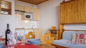 A cozy room with a wooden table set for dining, a bed with striped bedding, and a wooden cabinet above the bed. - Les Genepis (Val Claret) by Interhome (Tignes)